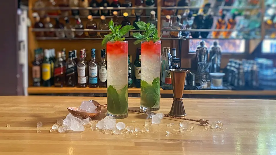 Two Apple Julep cocktails next to a measuring glass and crushed ice